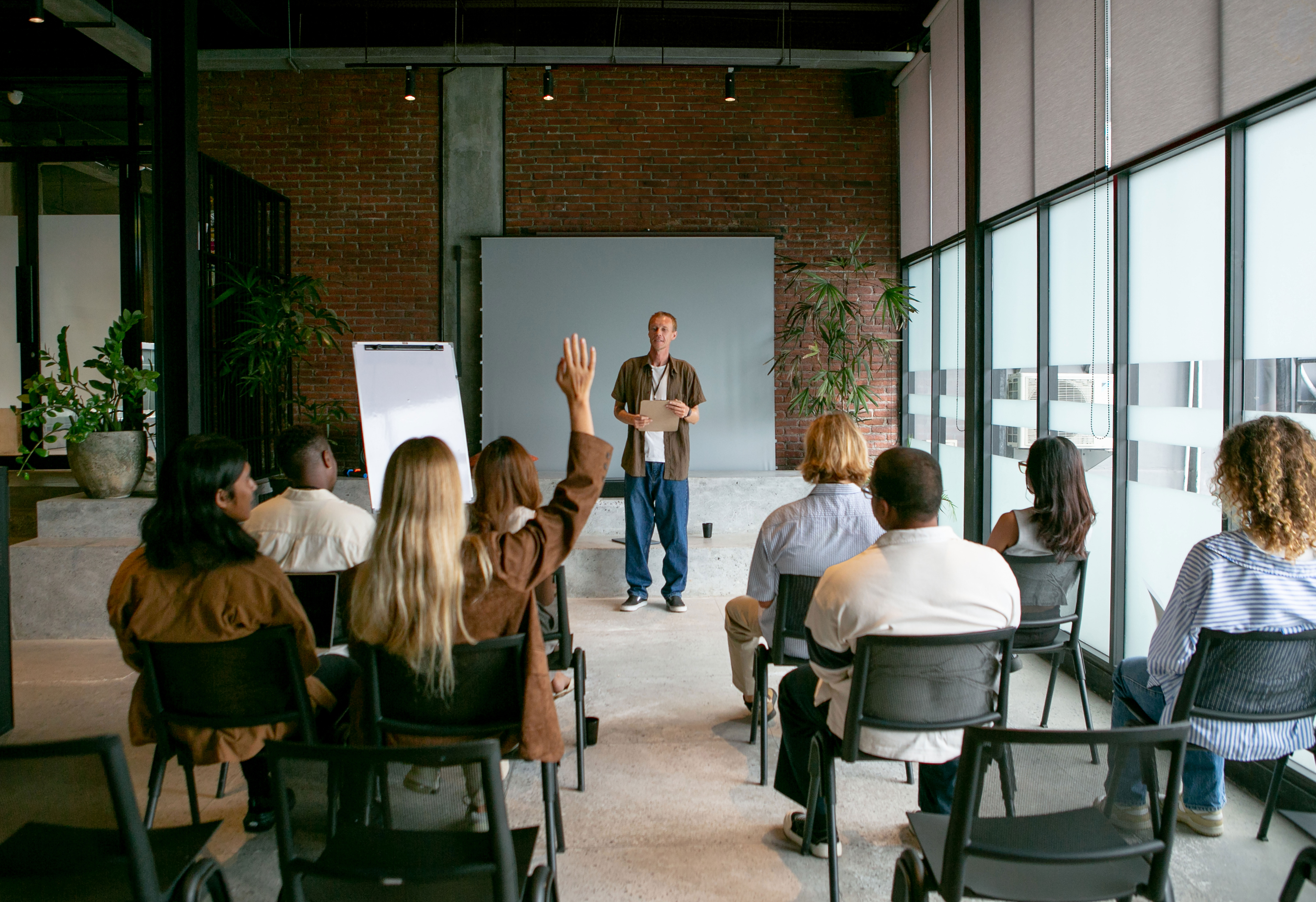 Workshop in einem Seminarraum: Teilnehmende hören einem Referenten zu, eine Teilnehmerin meldet sich